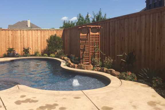Landscaping with boulder stone rocks around Frisco, TX swimming pool with cedar arbor and low maintenance plants and trees designed by Sol Vida Landscaping company.